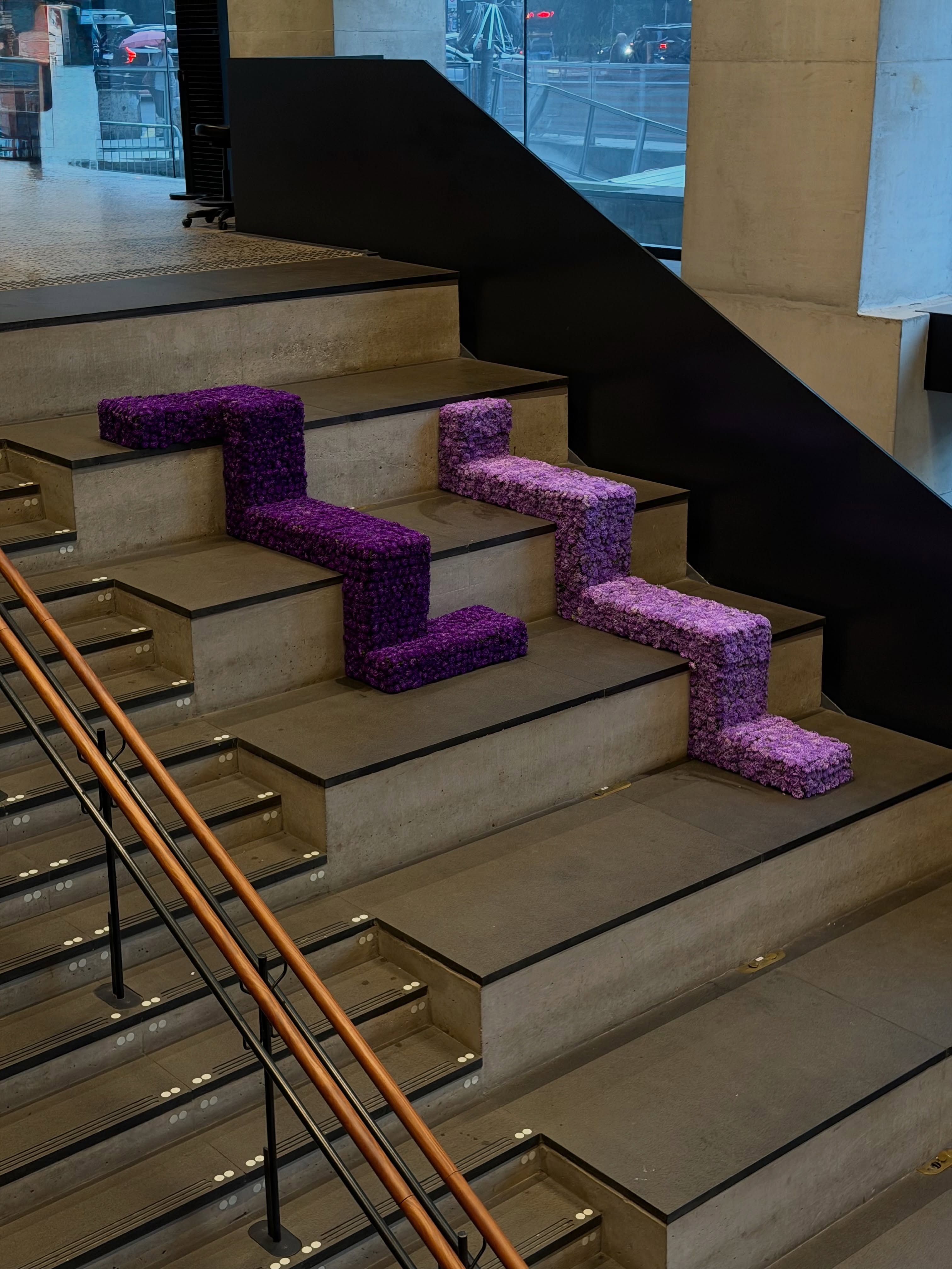 Instalações geométricas feitas com flores roxas acompanhando os degraus de uma escada.
